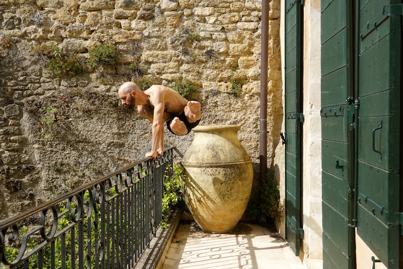 Daniel in a green vest jumps in mid air with his left leg higher then his right creating a long diagonal